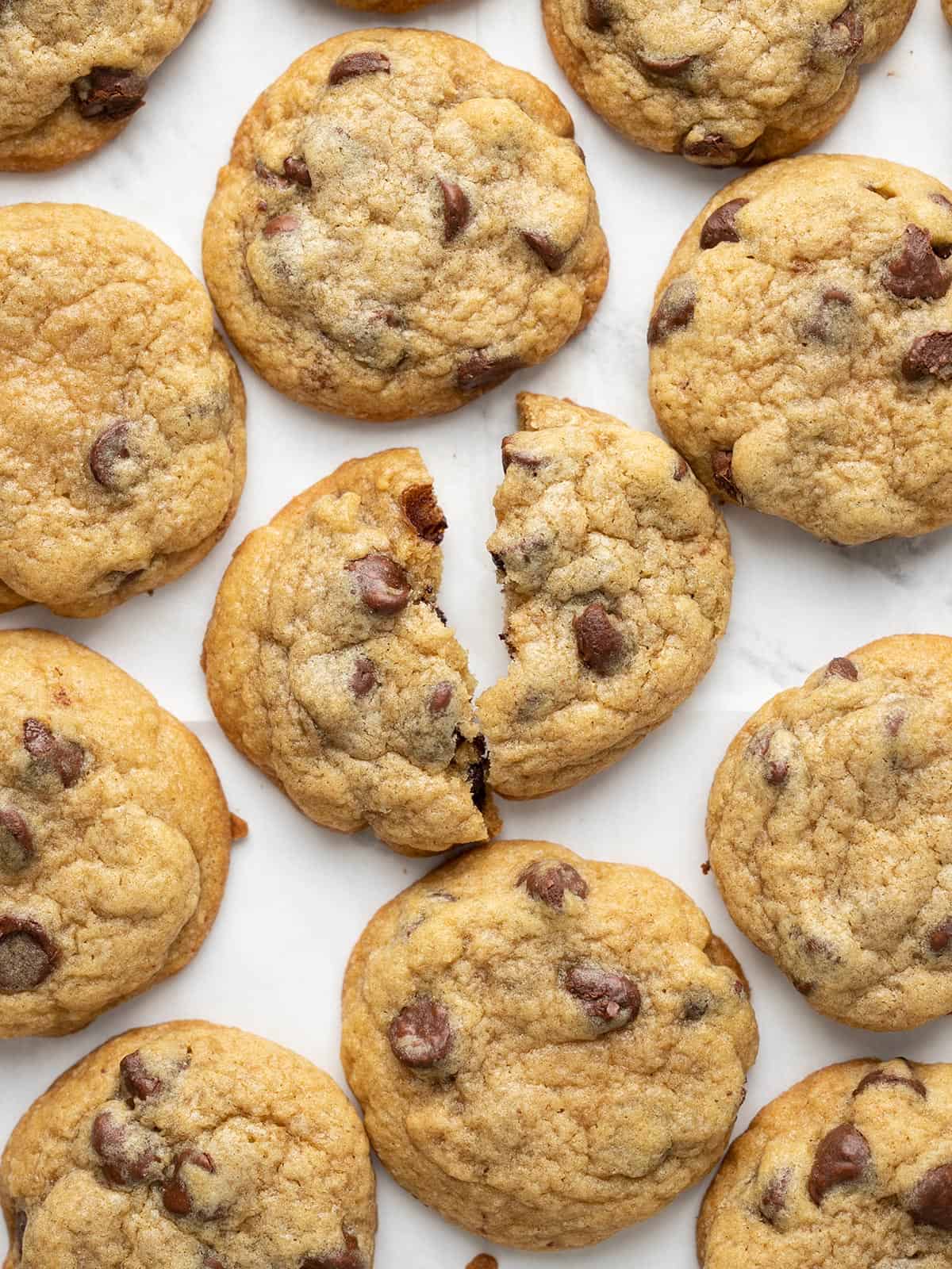 Overhead view of chocolate chip cookies on a white surface, one broken in half.