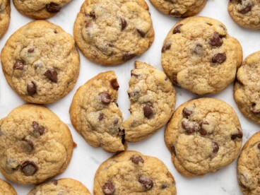 Overhead view of chocolate chip cookies on a surface, one broken in half.