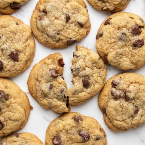 Overhead view of chocolate chip cookies on a surface, one broken in half.