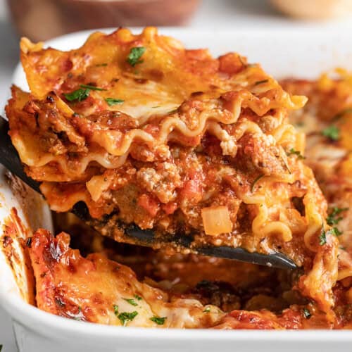 Close up side view of a slice of homemade lasagna being lifted from the casserole dish.