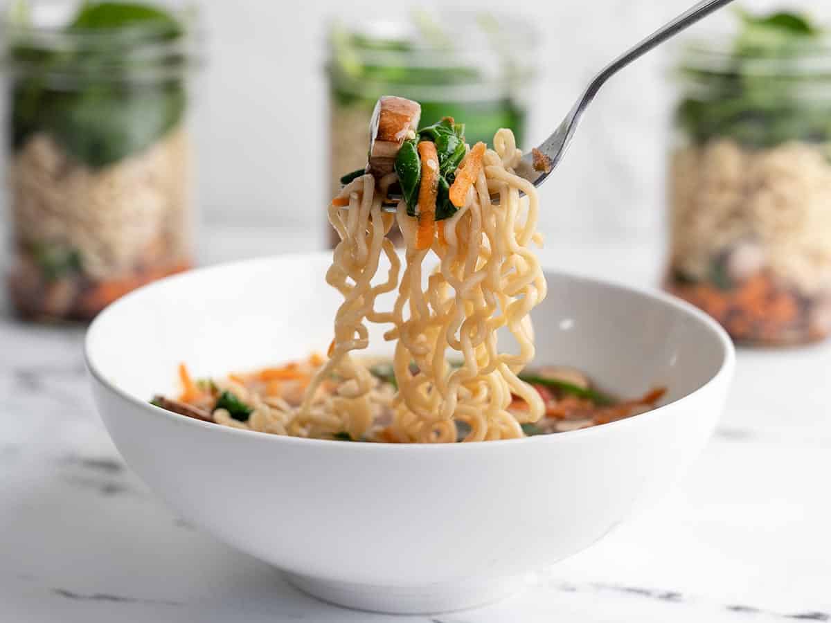 A fork lifting noodles out of a bowl with the jars in the background. 