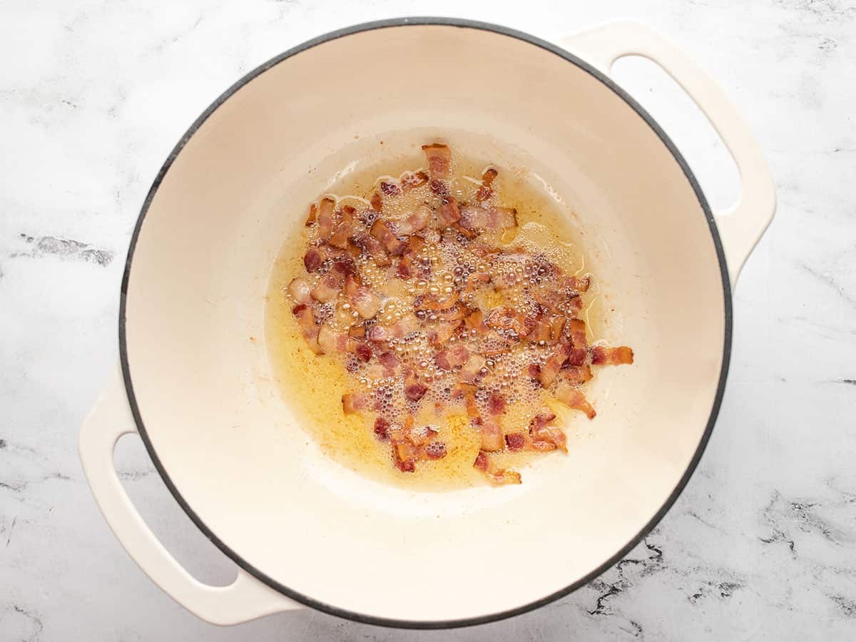 Small slices of bacon frying in the bottom of a large dutch oven.