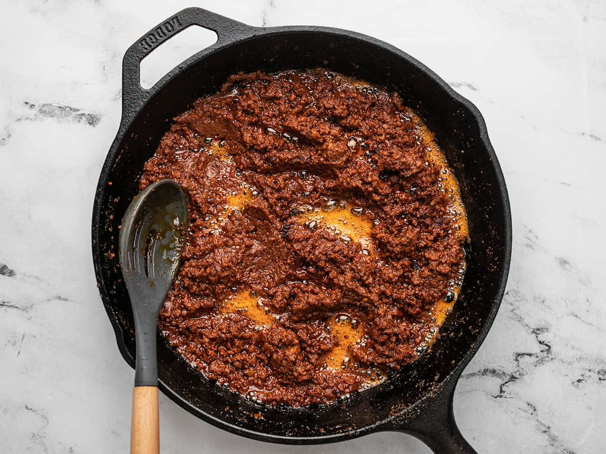 Overhead shot of chorizo cooking in a cast iron pan with a slotted spoon in it.