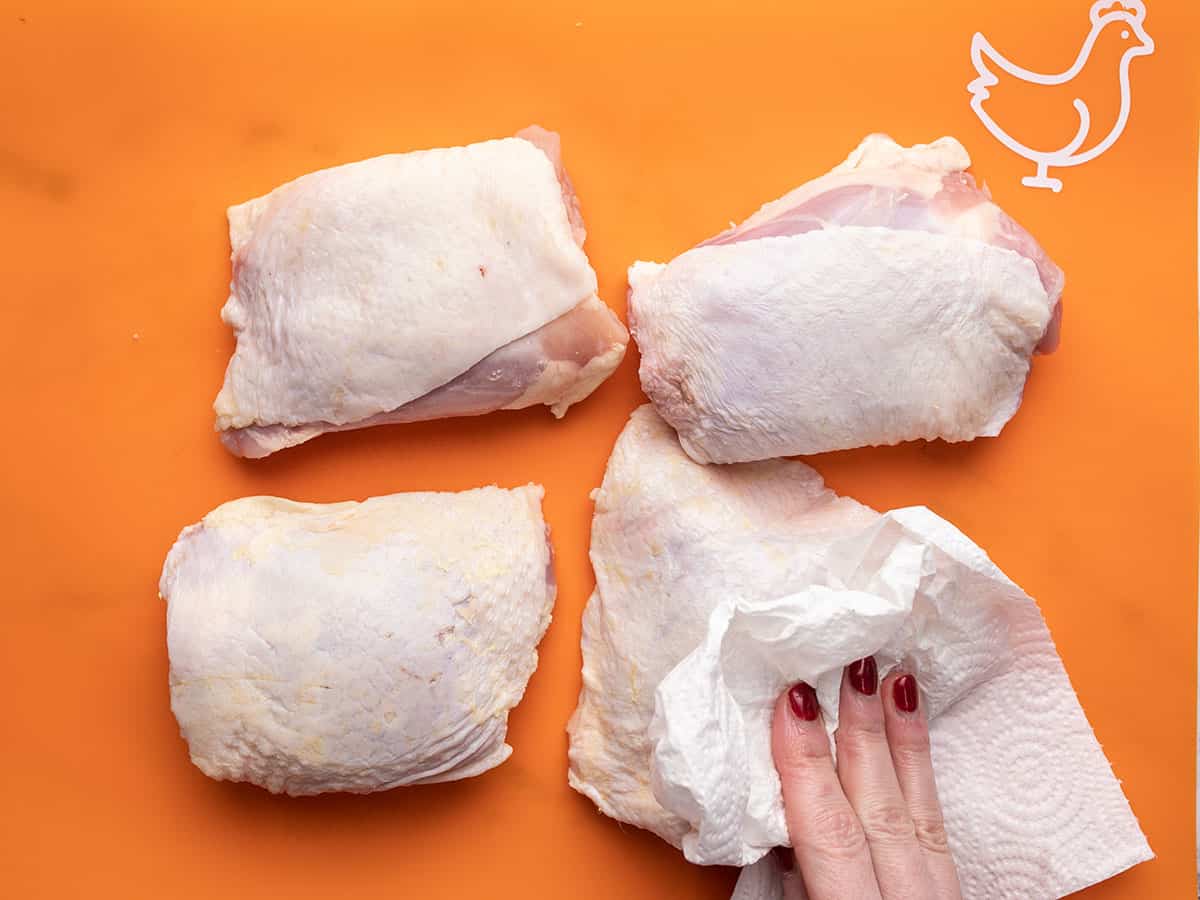 Chicken thighs being patted dry with paper towel.