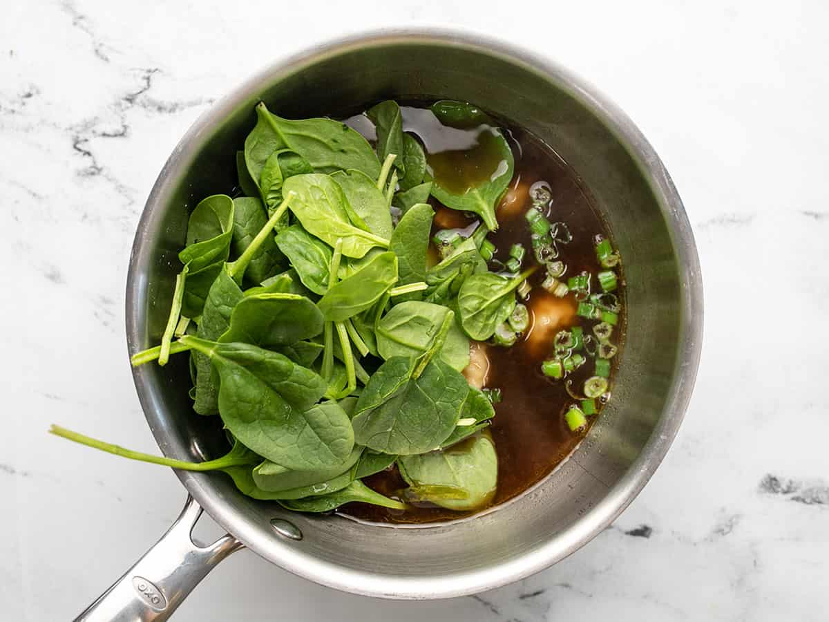 A pile of fresh spinach sitting on top of a pot full of warm dumpling soup.