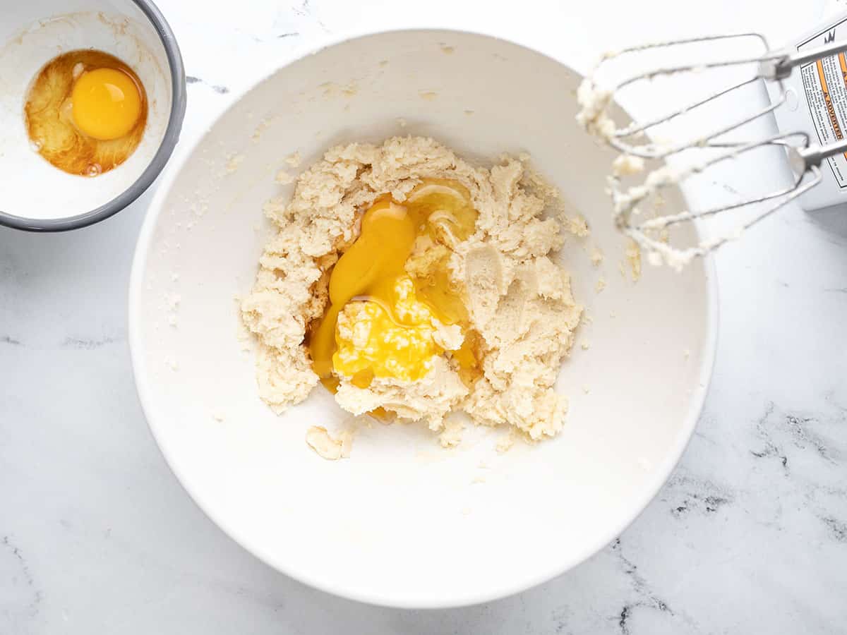 Egg and vanilla being mixed into creamed butter in a white bowl.