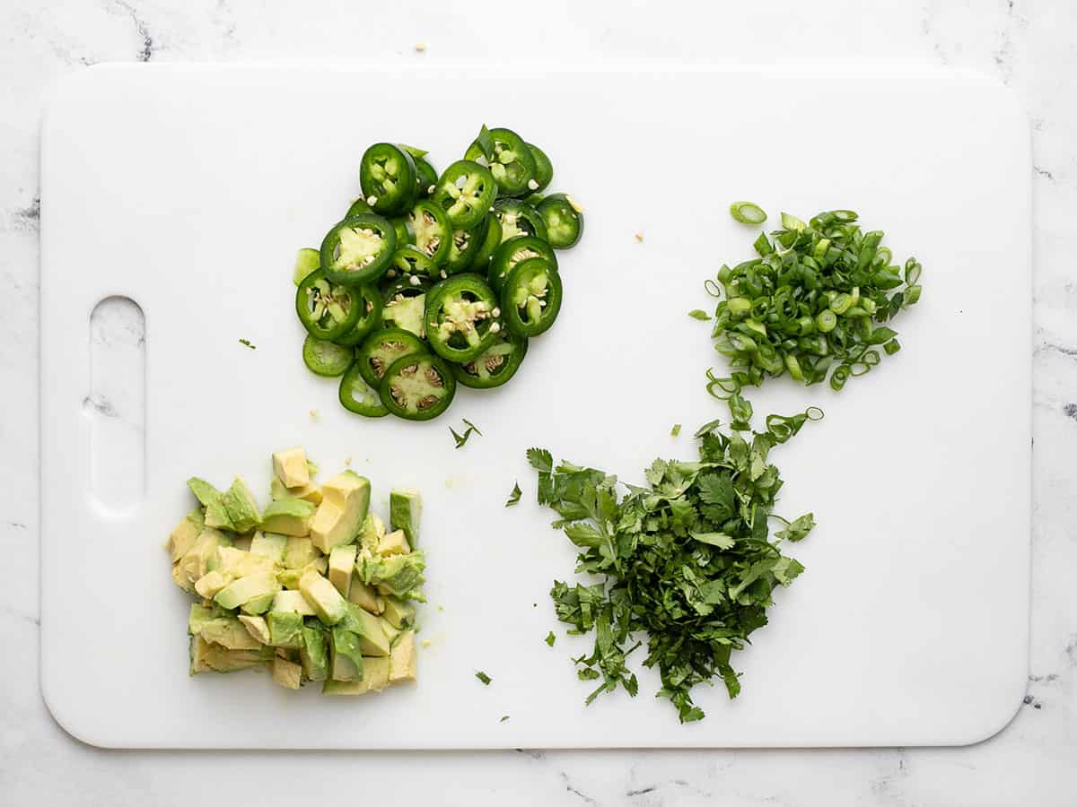 Overhead shot of chopped toppings on a white cutting board.