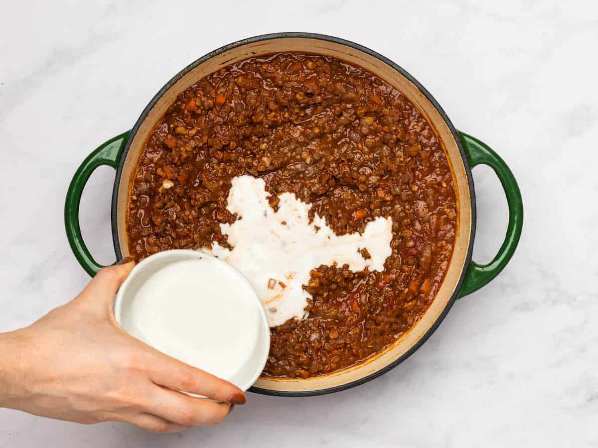 Coconut milk being poured into the sauce in the pot. 