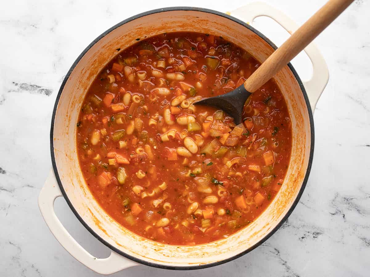 Finished Pasta e Fagioli soup with a wooden spoon sticking out of the top right side of the pot. 