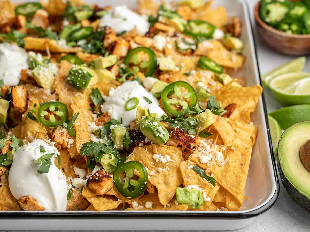 Forty five degree angle shot of sheet pan chicken nachos with sliced jalapeño, avocado, and cilantro.