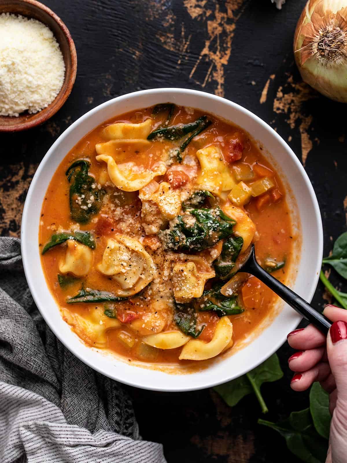 Overhead view of a bowl full of tortellini soup with a spoon lifting a bite.