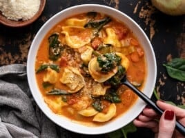 Overhead view of a bowl of creamy tortellini soup with a spoon in the side.