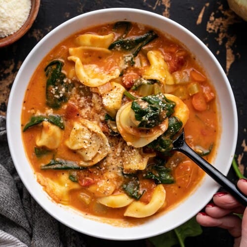 Overhead view of a bowl of creamy tortellini soup with a spoon in the side.