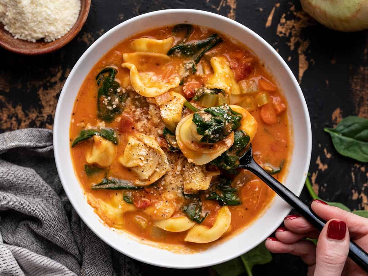 Overhead view of a bowl of creamy tortellini soup with a spoon in the side. 