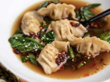 A close up view of dumpling soup in a white bowl topped with white sesame seeds and chili crisp.