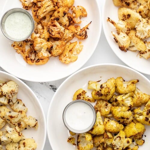 Four plates full of roasted cauliflower with dipping sauce.