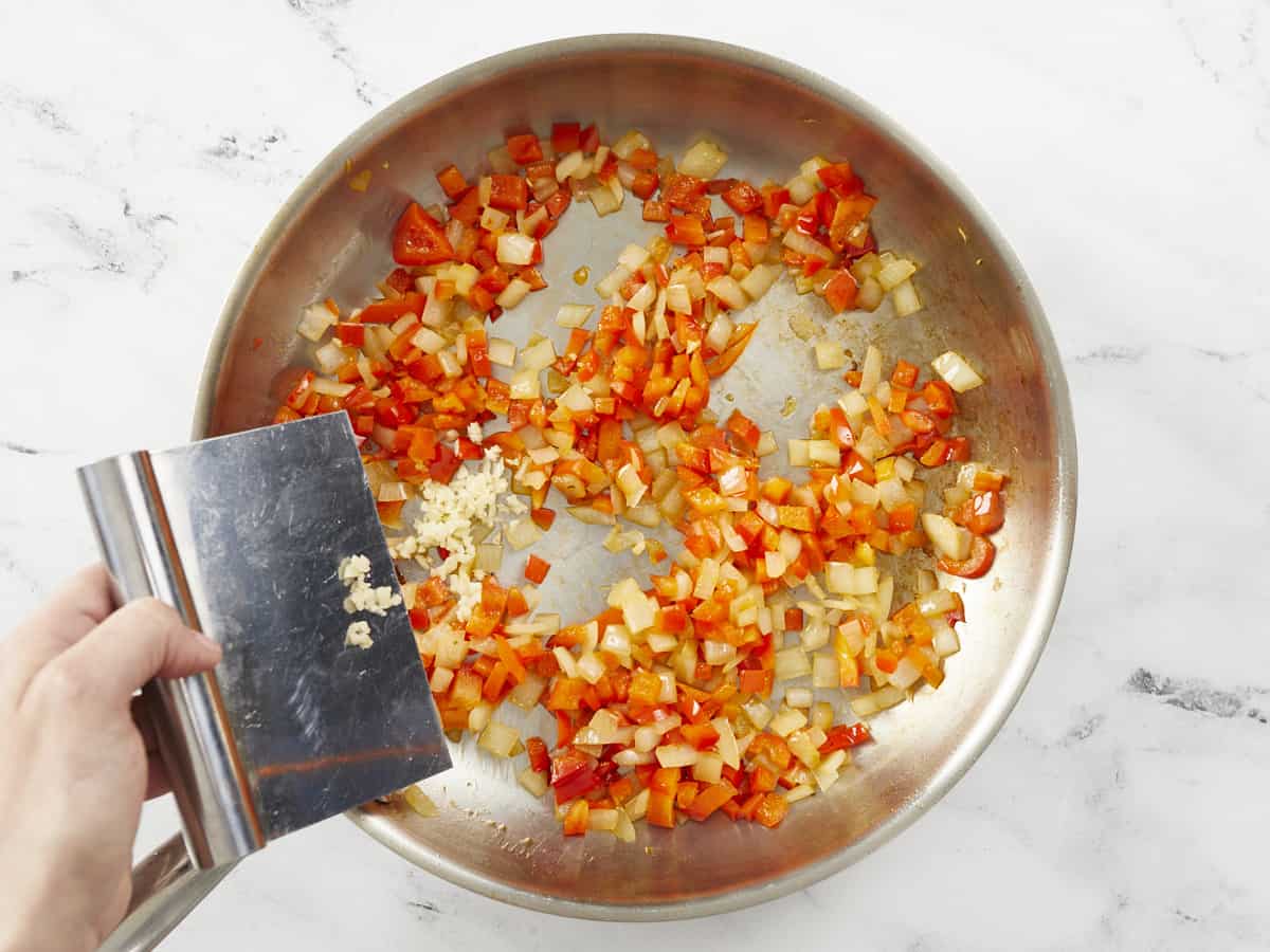 Overhead shot of garlic being added to a pan of onions and peppers.