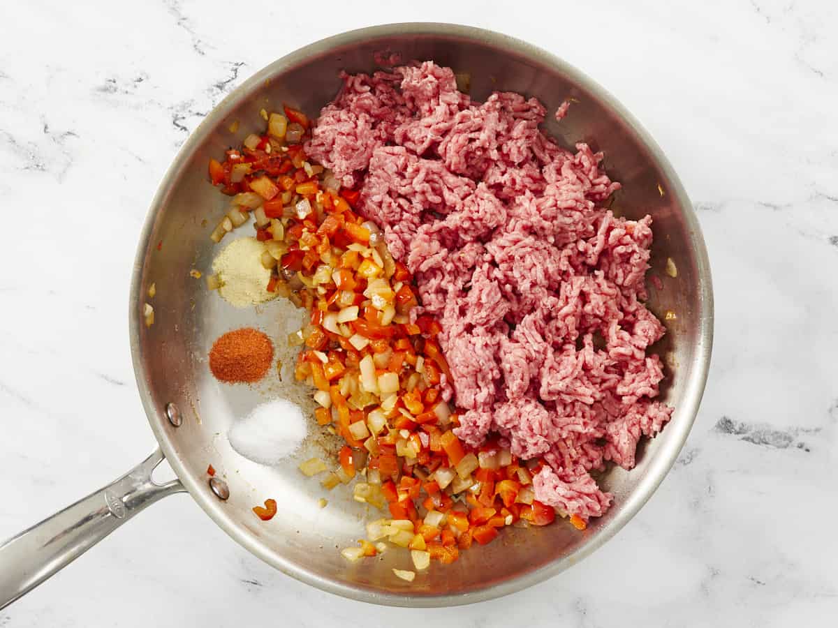 Meat being added to a pan of garlic, onions, and peppers.