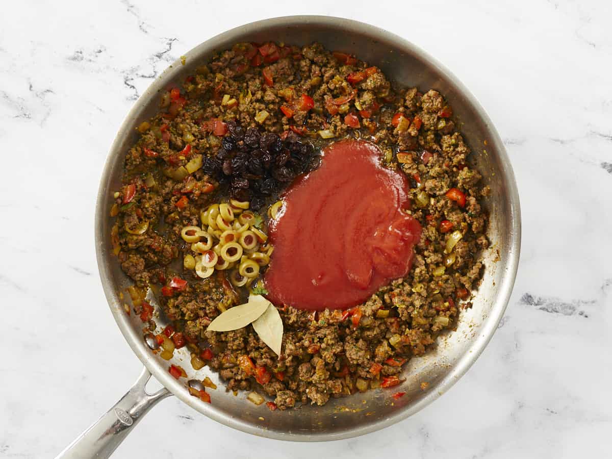 Tomato sauce, olives, and raisins added to a pan of browned meat and sofrito.