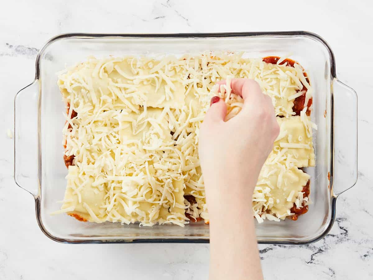 Cooked ravioli in the dish, cheese being sprinkled over top.