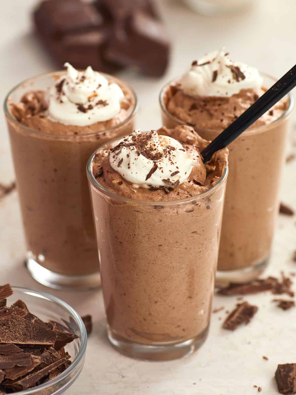 Side view of three cups of chocolate mousse, one with a spoon in the center.