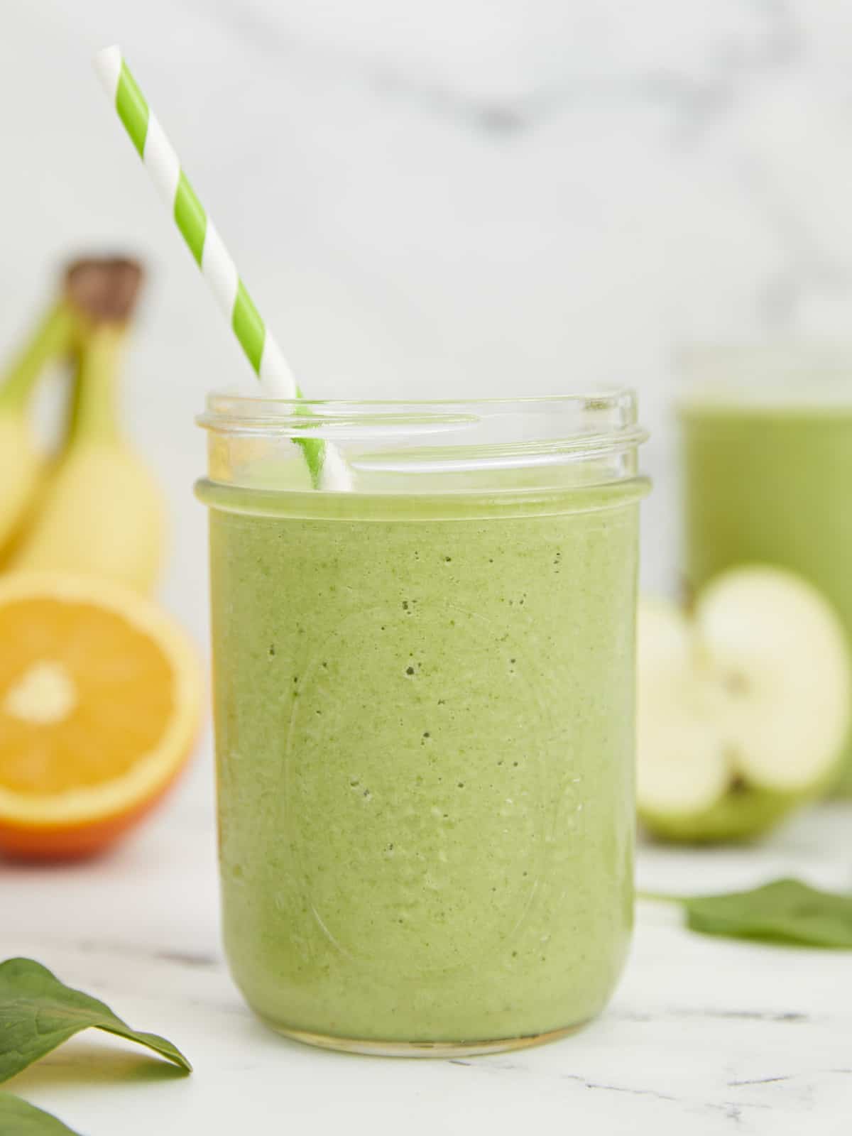 Side shot of green smoothies surrounded by cut fruit.