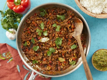 Overhead shot of picadillo in a silver skillet with a wooden spoon in it.