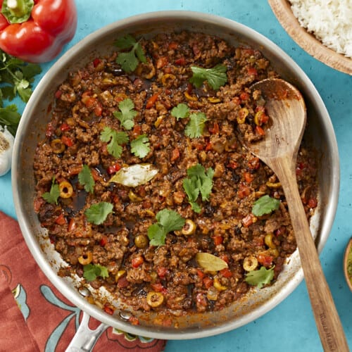 Overhead shot of picadillo in a silver skillet with a wooden spoon in it.