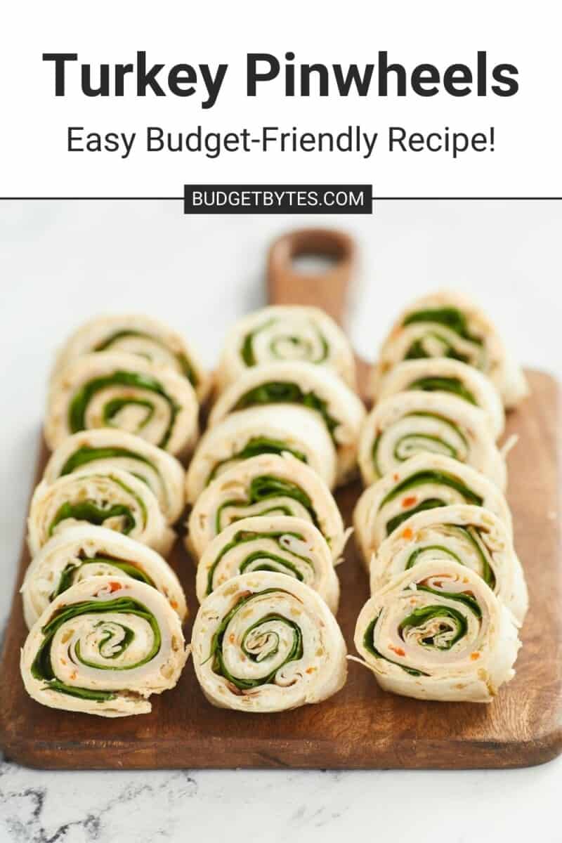 Eighteen turkey pinwheels lined up into three rows on a wooden cutting board against a white marble background.