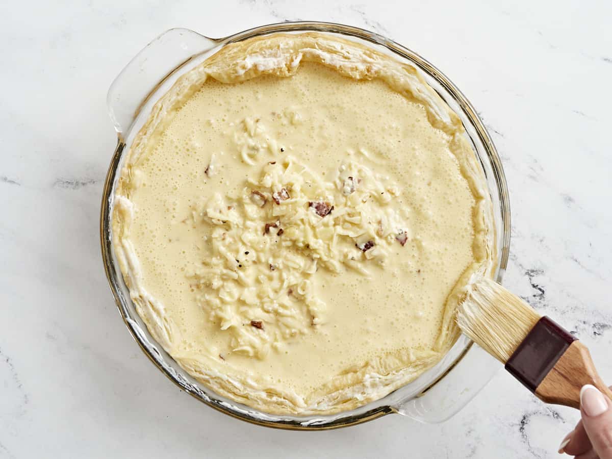 Overhead shot of cream being brushed on puff pastry.