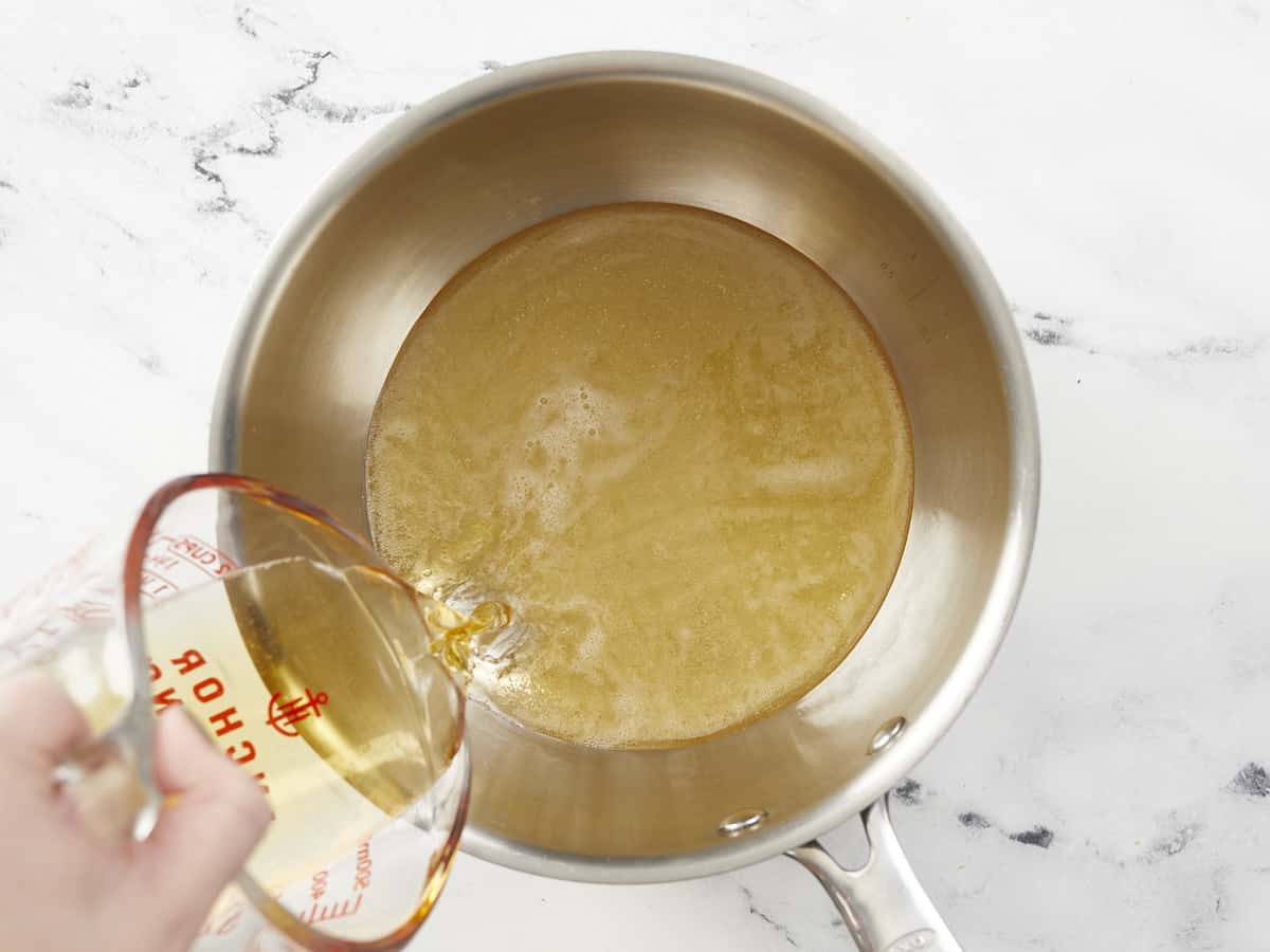 A small saucepot being filled with beer from a glass measuring cup held above the bottom right corner of the pot.