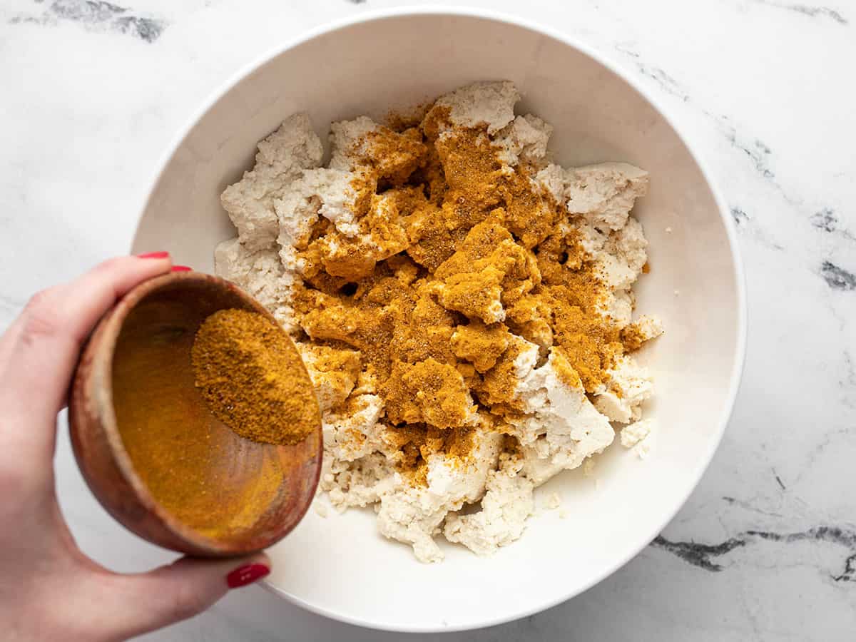 Spices being sprinkled over the bowl of tofu.