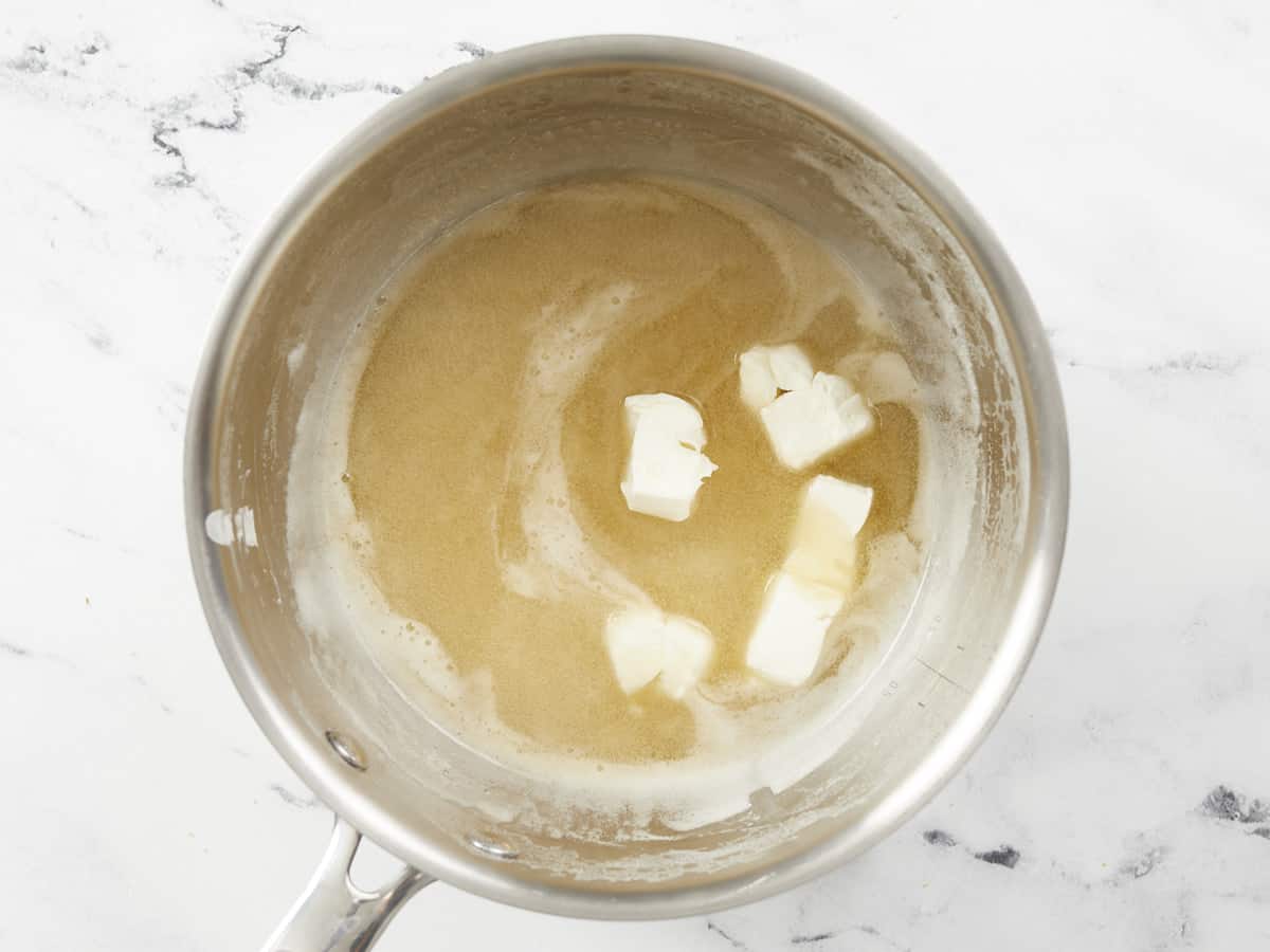 A small saucepot of boiled beer with chunks of unmelted cream cheese in the right side of the pot ready to be mixed into the beer.