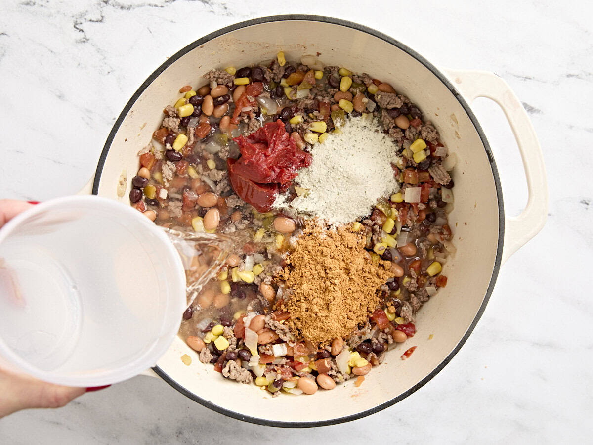 Water and seasonings added to beans to make taco soup in a dutch oven.