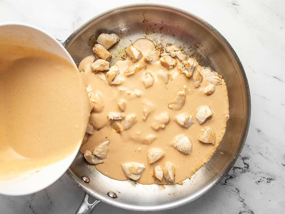 Peanut sauce being poured into the skillet with the chicken.