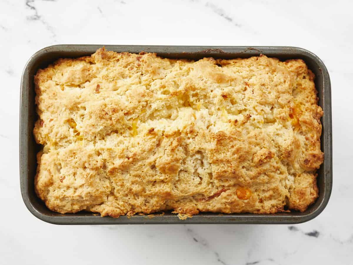 A horizonal image of a baked loaf of bread with a golden-brown, crunchy top in metal loaf pan.