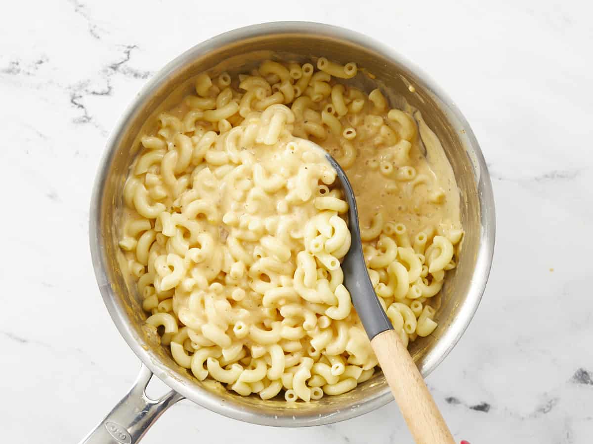 Cooked macaroni being stirred into the cheese sauce.