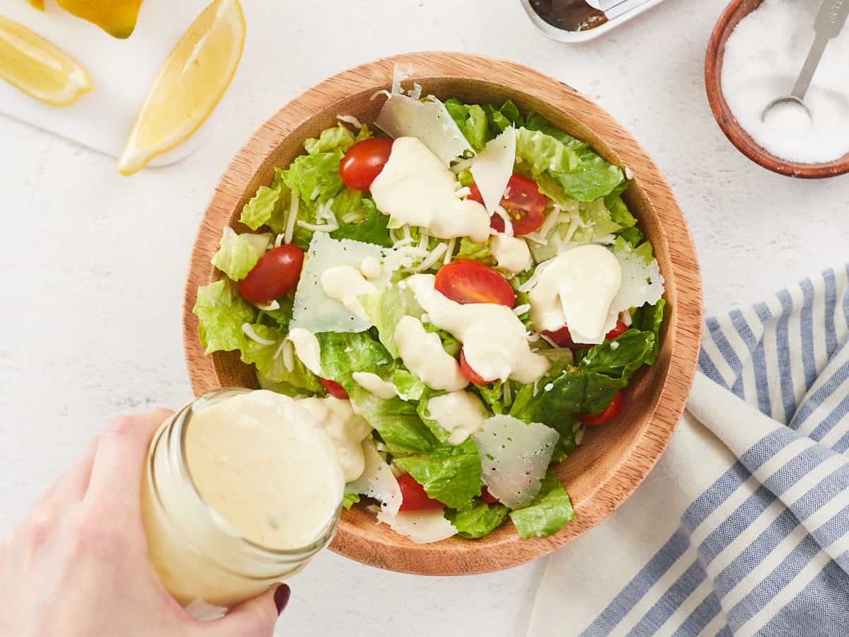 Caesar dressing being poured over a salad.