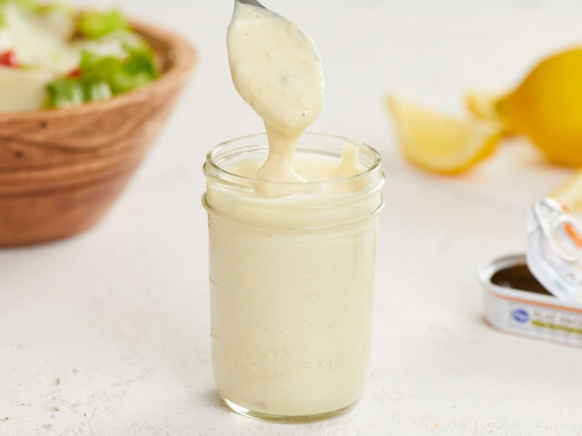 Caesar dressing dripping off a spoon into a jar.