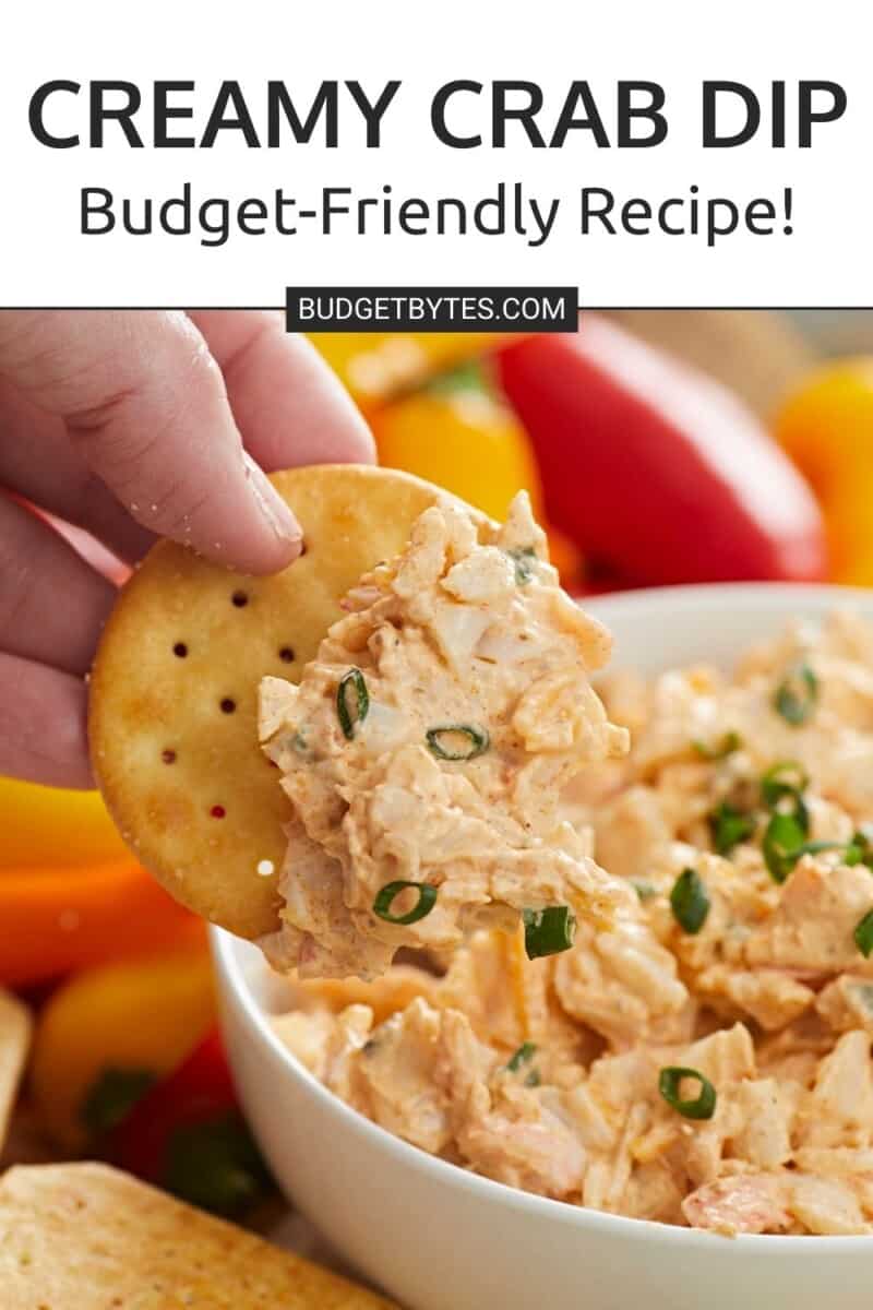 Hand dipping cracker in a bowl of crab dip.