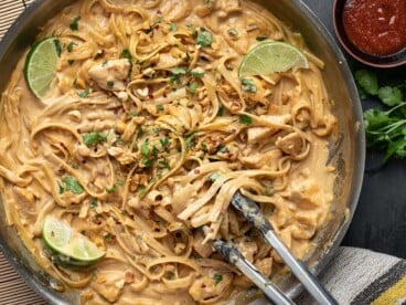 Close up overhead view of peanut noodles in the skillet with tongs.