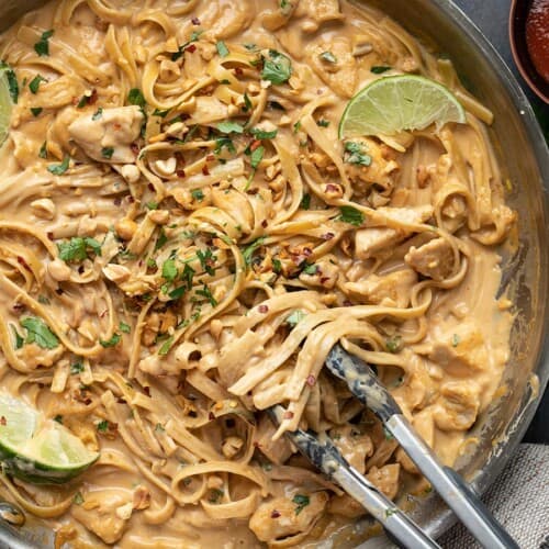 Close up overhead view of peanut noodles in the skillet with tongs.