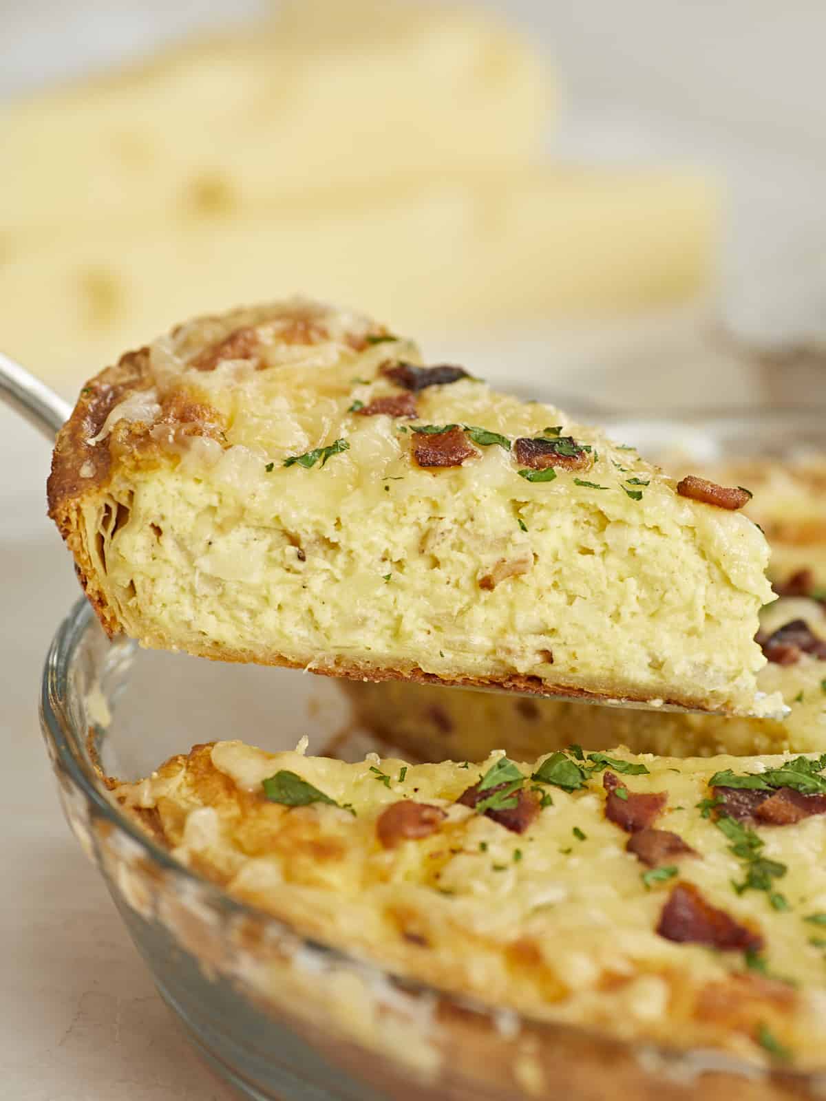 Side shot of a slice of Quiche Lorraine being lifted out of the pie plate.