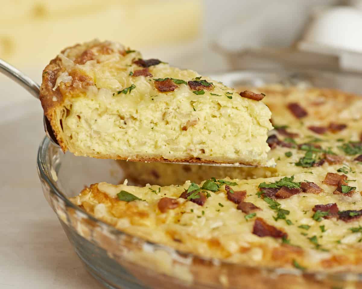 Side shot of a slice of Quiche Lorraine being lifted out of the pie plate.