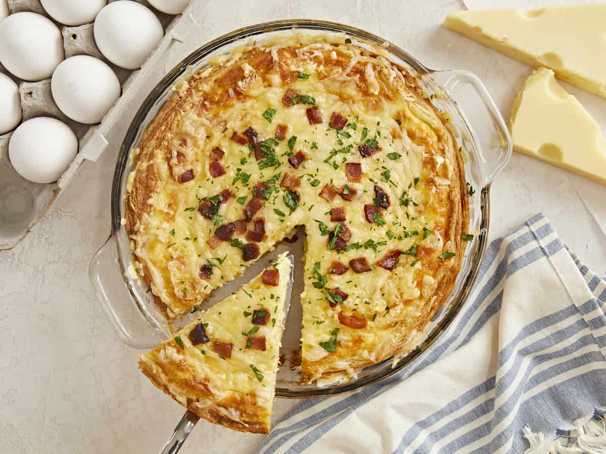 Overhead shot of a slice of Quiche Lorraine being lifted out of the pie plate.