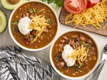 Overhead view of two bowls of taco soup, topped with sour cream and shredded cheese.