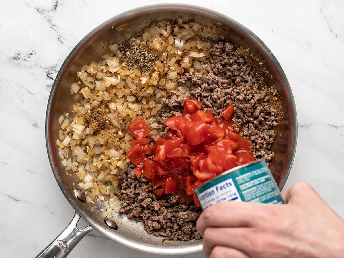 Overhead shot of beef and tomatoes added to onions in silver sauté pan.