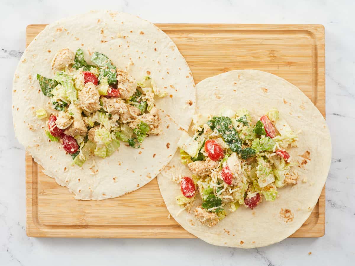 Chicken caesar wraps filled but not rolled on a wooden cutting board.