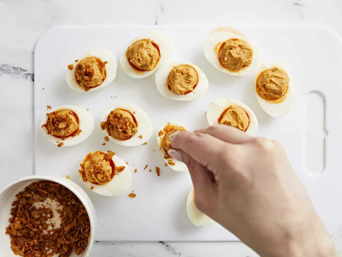 Overhead shot of finished Nashville Hot Deviled Eggs being sprinkled with crushed chips.