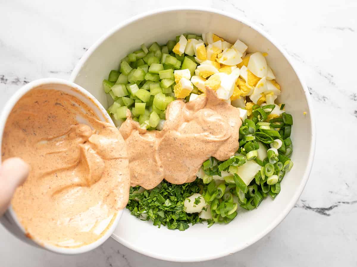 Dressing being poured over potato salad ingredients in the bowl. 